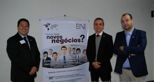 três homens de terno ao lado de faixa com os dizeres "Vamos fazer novos negócios?" durante jantar do BNI