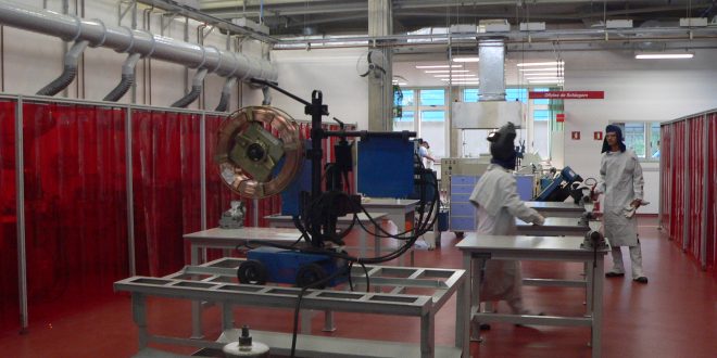 alunos trabalhando em mesas industriais entre máquinas vermelhos no SENAI