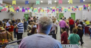 um tecladista visto de costas com o público à sua frente, em segundo plano, durante baile junino no Espaço Movimenta Cotia