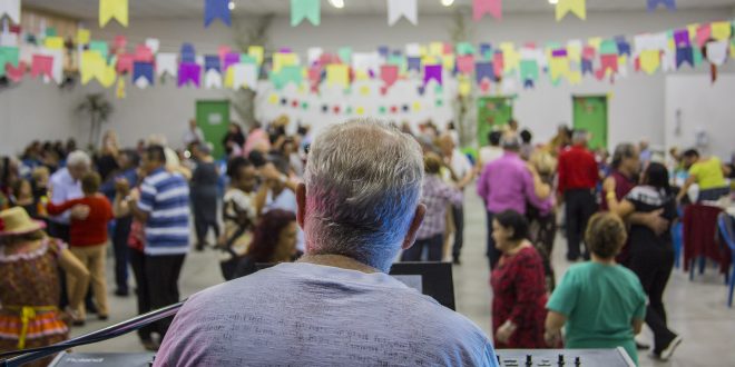 um tecladista visto de costas com o público à sua frente, em segundo plano, durante baile junino no Espaço Movimenta Cotia