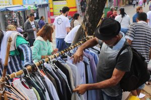 homem vasculha roupas penduradas em arara durante The Street Store em Carapicuíba