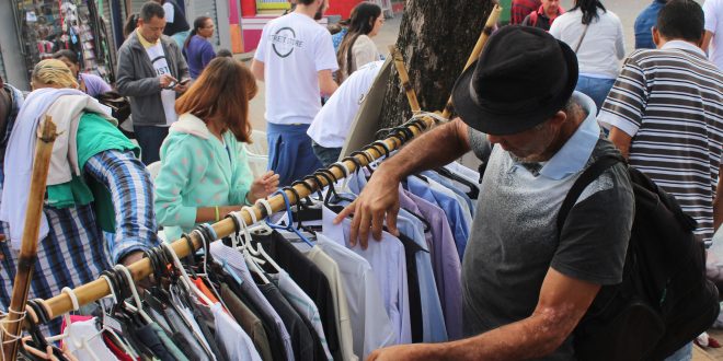 homem vasculha roupas penduradas em arara durante The Street Store em Carapicuíba