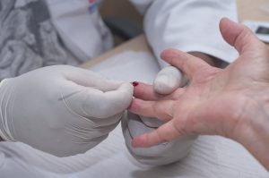 close da mão de uma pessoa tendo uma gota de sangue extraída por duas mãos médicas