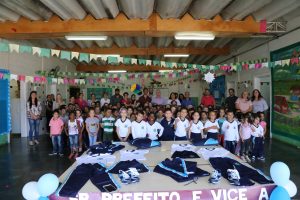 alunos posam para foto atrás de mesa com kits de uniformes escolares novos