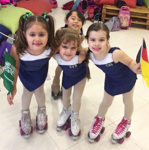 três pequenas alunas de Paula Donati posam sorridentes e com patins nos pés