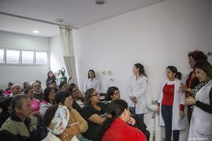 grupo de idosos acompanha explicações de profissionais de saúde em pequeno auditório
