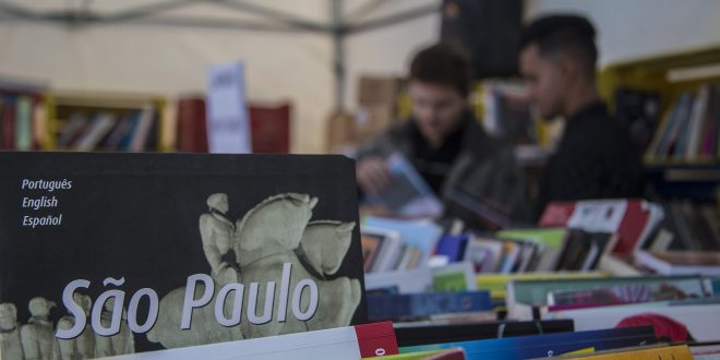 vários livros em primeiro plano, com algumas pessoas folheando-os em segundo plano