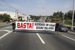 manifestantes caminham com faixa com os dizeres 'Basta! Queremos um lugar seguro pra viver'
