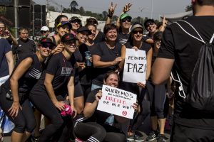manifestantes sorriem para uma câmera com cartazes escrito 'queremos paz' e 'queremos de volta nosso direito de ir e vir'