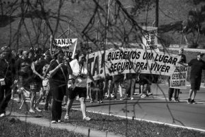 manifestantes caminham com faixa com os dizeres 'Basta! Queremos um lugar seguro pra viver'