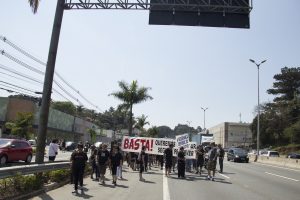 manifestantes caminham com faixa com os dizeres 'Basta! Queremos um lugar seguro pra viver'