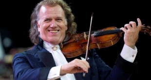 André Rieu de terno sorrindo e tocando violino