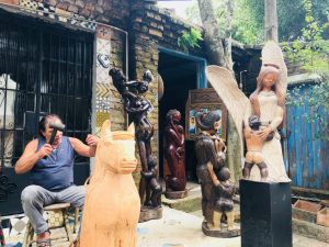 claudio veneranto esculpindo uma escultura em madeira, com diversas obras à sua volta