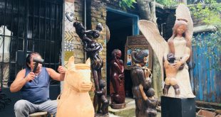 claudio veneranto esculpindo uma escultura em madeira, com diversas obras à sua volta