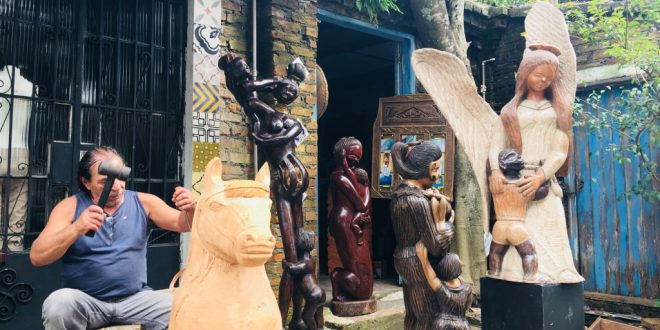 claudio veneranto esculpindo uma escultura em madeira, com diversas obras à sua volta