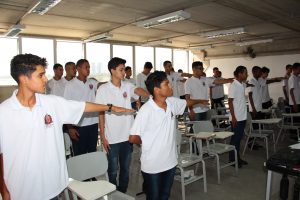 grupo de meninos em pé fazendo referência com o braço numa sala de aula