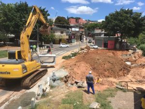 retroescavadeira trabalhando em grande buraco com bairro ao fundo