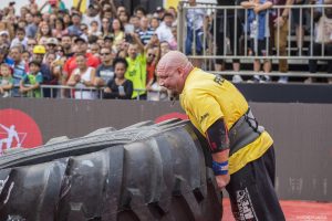 um homem tenta virar um grande pneu de caminhão durante o força bruta