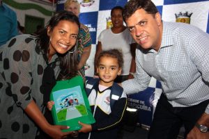 prefeito marcos neves, vice-prefeita gilmara gonçalves e uma aluna posam com material em mãos