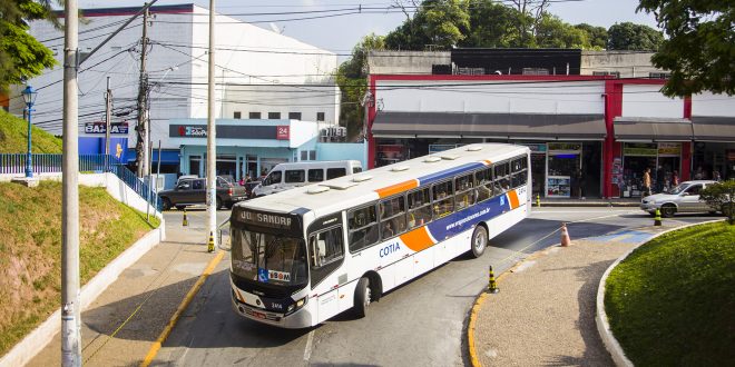 um ônibus de cotia visto de um viaduto, dobrando uma esquina e prestes a descer uma ladeira que passará embaixo da ponte