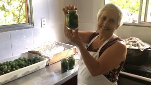 uma senhora exibe um alimento produzido por ela, dentro de um pote