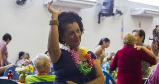 uma idosa com um colar de flores havaiano dançando num baile da terceira idade de cotia