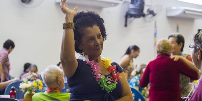 uma idosa com um colar de flores havaiano dançando num baile da terceira idade de cotia