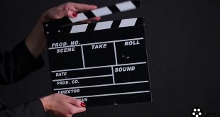 uma claquete sendo segurada por um par de mãos ante um fundo negro