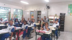 alunos da EM Professora Otília Freire Shimada com as mãos levantadas e sorrindo para a câmera em sala de aula