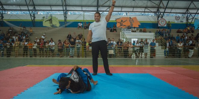 dois atletas no tatame enquanto um árbitro faz orientações