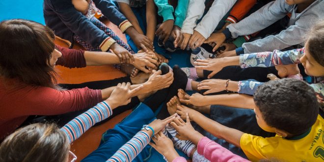 crianças sentadas em círculo com as pernas esticadas e roçando os pés