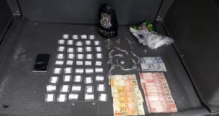 drogas e cédulas de dinheiro dispostos em mesa com bracelete da gcm ao lado