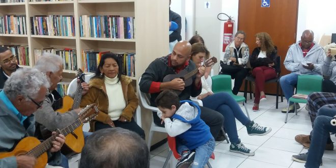 músicos com violão e pessoas sentadas acompanham sarau na biblioteca batista cepelos
