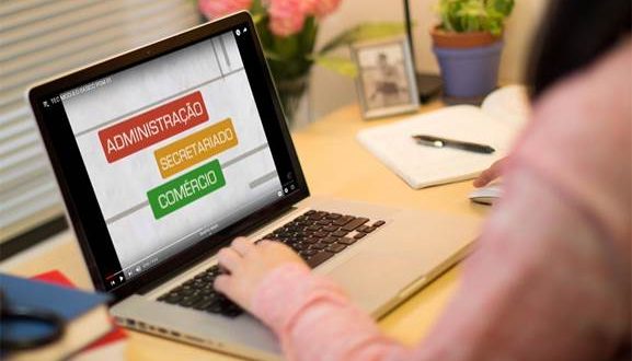 uma mulher consultando um notebook com os dizeres 'administração, secretariado, comércio' na tela e apenas os seus braços mostrados