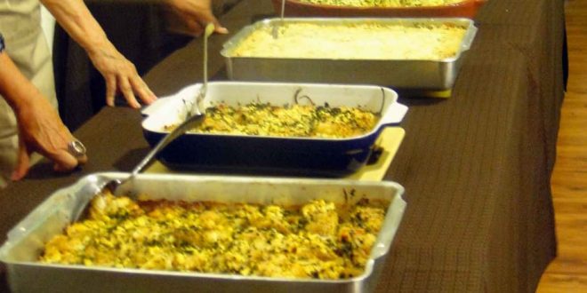 diversas travessas com comidas portuguesas dispostas em uma mesa com mulheres prontas para servir convidados