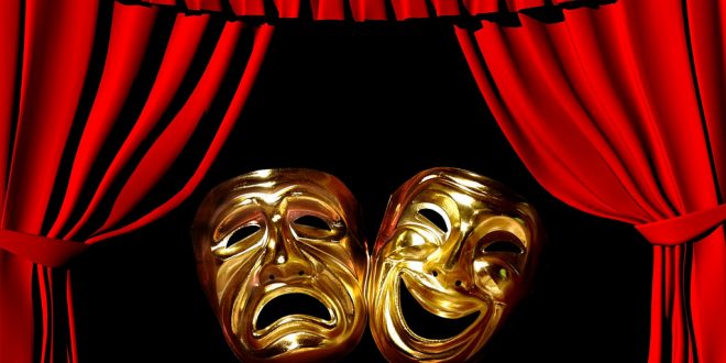 uma máscara alegre e outra feliz ante um fundo preto rodeado por cortinas vermelha de um palco
