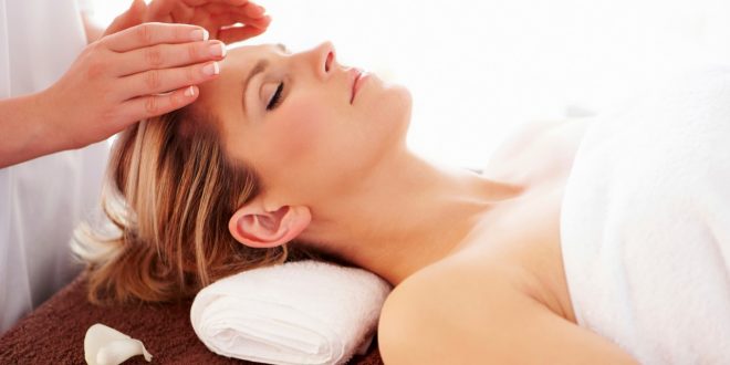 uma mulher deitada e de olhos fechados com um par de mãos sobre sua face realizando um procedimento reiki